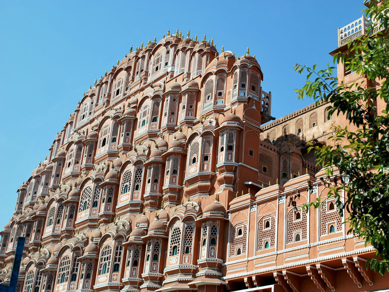 Rosa Fassade des Hawa Mahal in Jaipur mit vielen kleinen Fenstern unter blauem Himmel.