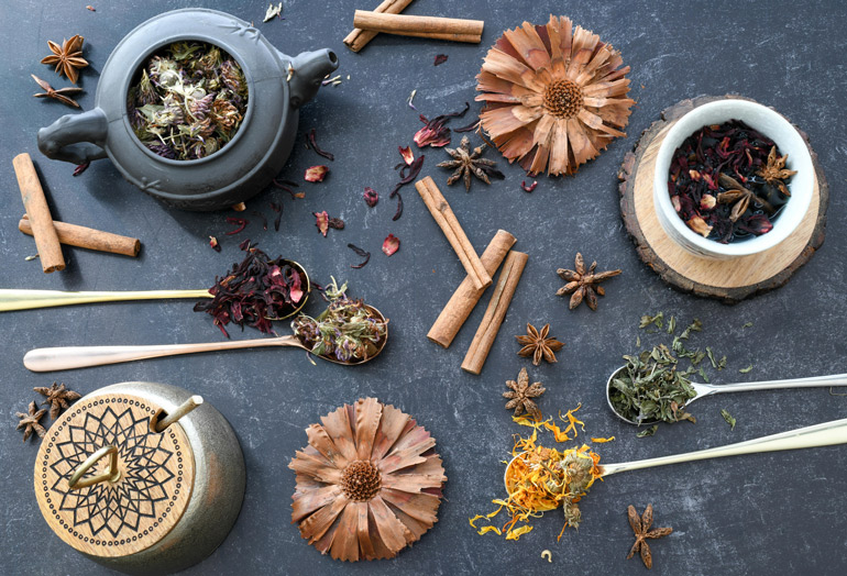 Ayurvedische Kräuter, Zimt, Sternanis und Teekannen auf dunkelgrauem Untergrund