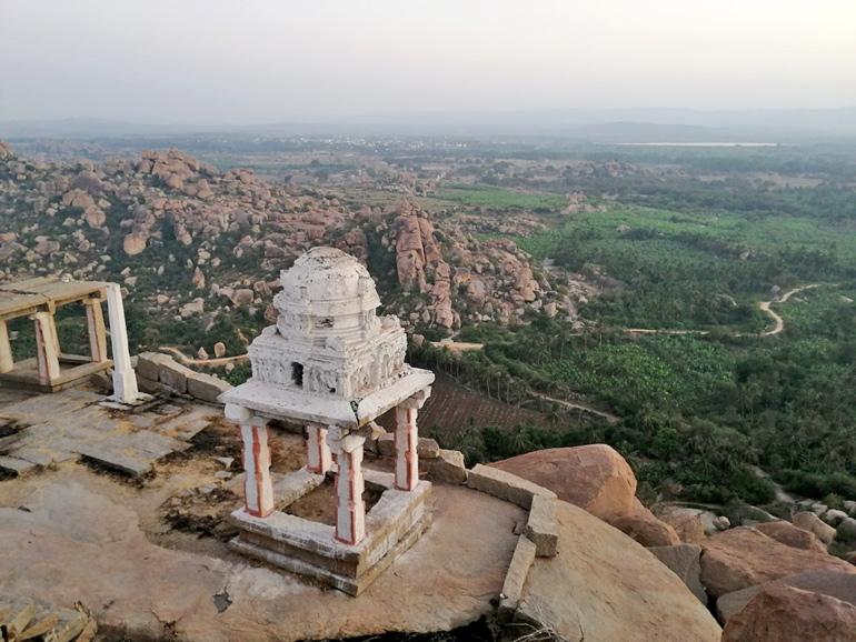 Kleiner weißer Schrein auf einem Felsen mit weitem Blick über das Tal von Hampi