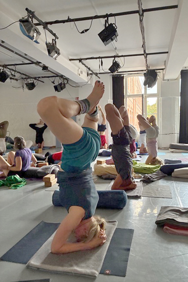 Yoga-Praktizierende im Kopfstand in einem Studio mit Scheinwerfern unter der Decke.