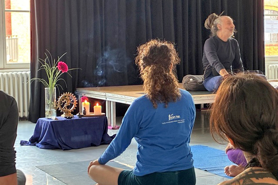 Yoga-Unterricht mit Lehrerin auf dem Podium, Altar mit Kerzen und Räucherstäbchen