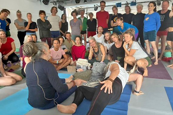 Yoga-Lehrer und ein Schüler demonstrieren eine Übung vor den Workshop-Teilnehmenden.