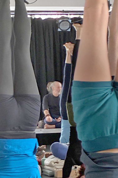 Detailansicht von Yoga-Übenden im Kopstand, im Hintergrund sitzend der Lehrer.